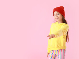 Adorable little girl in yellow hoodie pointing at something on pink background