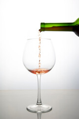 red wine from a bottle is poured into a glass on a light background. alcoholism and addiction. drinks for the holiday