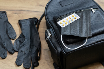 Women's backpack bag and a medical mask with medicines in an open pocket next to medical gloves