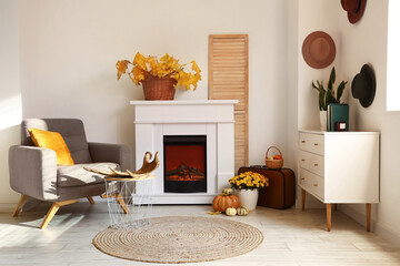 Interior of light room with modern fireplace, armchair and chest of drawers