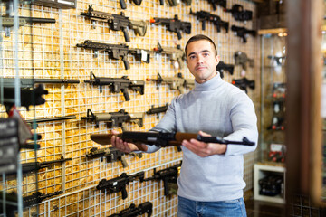Man standing in salesroom of airsoft shop and holding assault rifle.