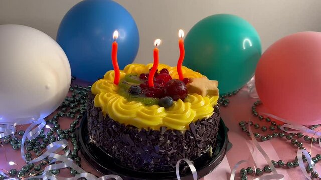 Happy birthday cake with burning red candles and colorful air balloons