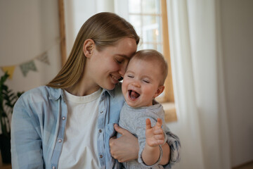 Portrait of young smiling mother holding and embracing her baby. Happiness, love and care concept. Cute child singing song having fun at home