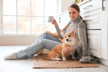 Young woman with cute Corgi dog and cup of tea in kitchen