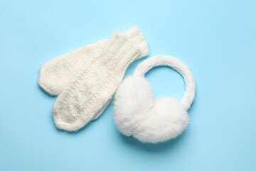 Knitted mittens and earmuffs on color background