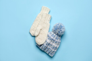 Knitted warm mittens and hat on color background