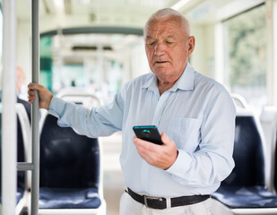 Fototapeta Old Caucasian man with smartphone standing in streetcar and waiting for next stop. obraz