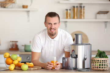 Fototapeta na wymiar Young man with glass of fresh fruit juice near modern juicer in kitchen