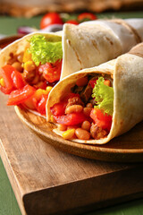 Board of tasty Mexican burritos with vegetables on green wooden background, closeup