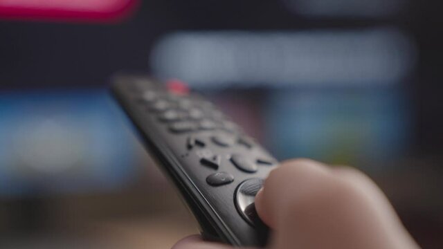 close-up of a caucasian hand with a TV remote switching channels, holding a TV remote control, flipping through channels and TV programs, looking for the desired movie in the cinema application