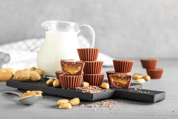 Board with tasty peanut butter cups and jug of milk on table