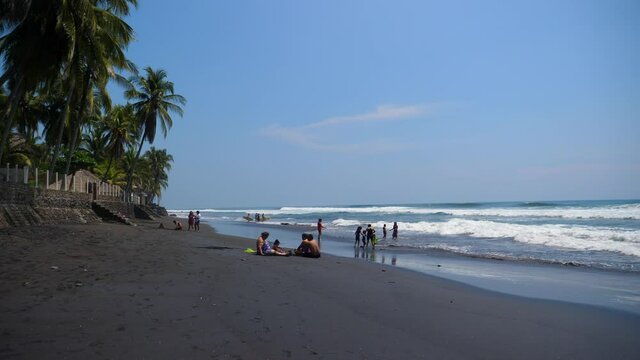 Full shot, scenic view of people on the shore on a bright sunny day on the bitcoin beach in El Salvador Mexico, waves and blue sky in the background.