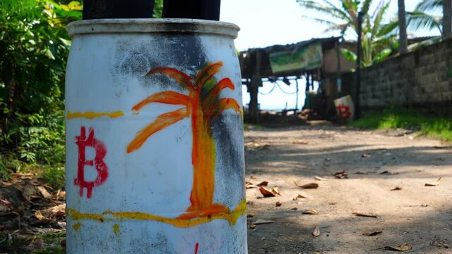 Close up focus shot, a white drum with a red bitcoin logo and orange tree drawing on the bitcoin beach in El Salvador, Mexico, another with drum with a bitcoin logo in the background.
