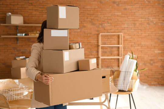 Woman holding cardboard boxes with belongings in office on moving day