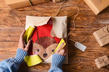 Woman in warm sweater unwrapping Christmas present on wooden background, closeup