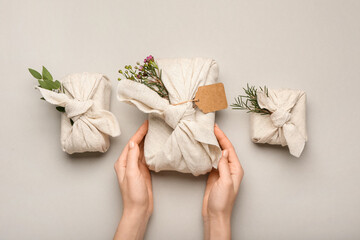 Female hands with beautiful gift boxes wrapped in fabric on light background, closeup