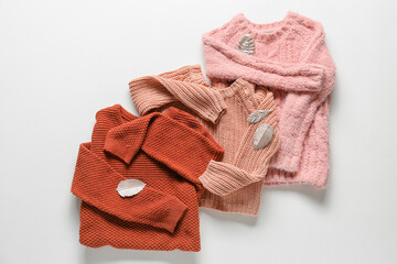 Folded kid sweaters and decorative feathers on white background