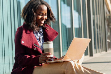 Happy young African woman consulting her social networks on a break from work having a coffee on...