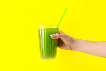 Woman holding glass of green juice on yellow background