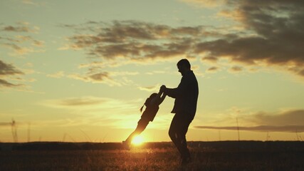 Fototapeta na wymiar Father circles hands of his beloved baby in sun on field, baby laughs in flight. Dad, child, daughter are playing in park at sunset. Healthy family and childhood. Happy family. Child have fun in