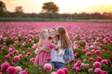 mother with two daughters on the background of a peony field. family at sunset background