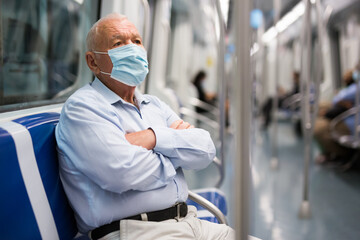 Fototapeta na wymiar Elderly man in face mask sitting on bench inside subway car and waiting for his stop.