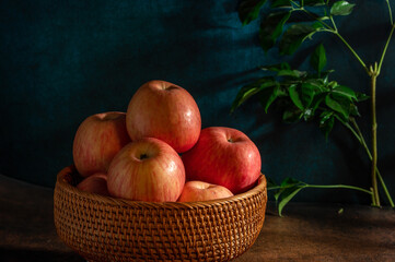 The apples on the plate look like oil paintings under the dim light on the wood grain table