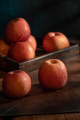 The apples on the plate look like oil paintings under the dim light on the wood grain table