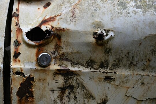 Close up of a door of an abandoned car in the forest, covered in rust and moss.   Bullet holes visible.