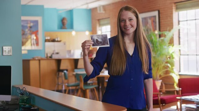 Wide portrait of pregnant new mother smiling at picture of sonogram in an urban loft space