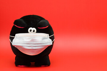 Cerdito de peluche color negro usando mascarilla sobre un fondo rojo. Concepto de protección....