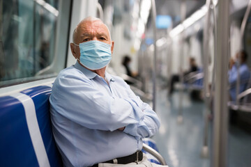 Fototapeta na wymiar Elderly man in face mask sitting on bench inside subway car and waiting for his stop.
