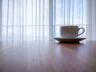 a coffee cup on the table beside the curtain window of the resort hotel  in the morning