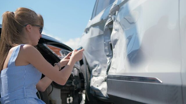 Stressed woman driver taking photo on mobile phone camera after vehicle collision on street side for emergency service after car accident. Road safety and insurance concept