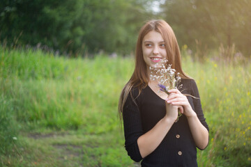 Young woman with a small bouquet of wild flowers outdoors.