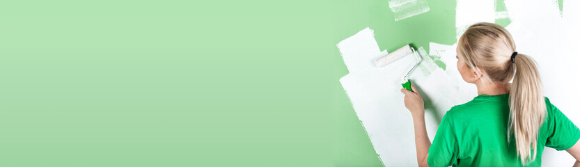 Young woman paints the wall in white colour. Long banner