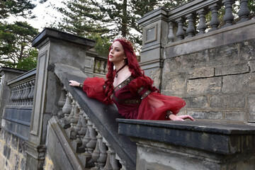  portrait of pretty  female model with red hair wearing glamorous renaissance red ballgown.  Posing...