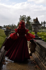  portrait of pretty  female model with red hair wearing glamorous renaissance red ballgown.  Posing in a fairytale castle location with staircases 