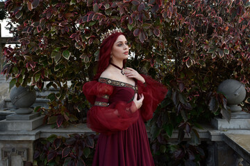  portrait of pretty  female model with red hair wearing glamorous renaissance red ballgown.  Posing in a fairytale castle location with staircases 