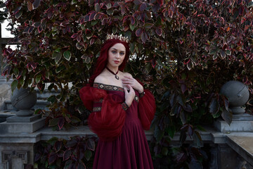  portrait of pretty  female model with red hair wearing glamorous renaissance red ballgown.  Posing in a fairytale castle location with staircases 