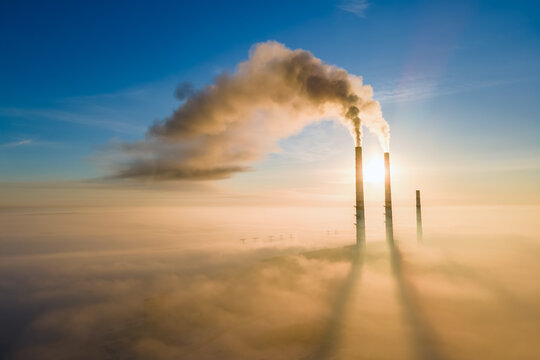 Aerial view of coal power plant high pipes with black smoke moving up polluting atmosphere at sunset