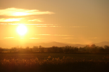 Beautiful evening panoramic landscape with bright setting sun over distant mountain peaks and asphalt road in front at sunset