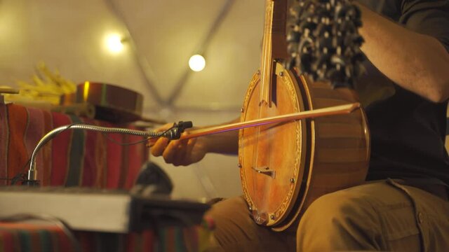 Close up person playing middle eastern turkish spike fiddle inside lighting tent during show