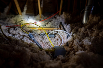 Electrical wire and conduit laying loose on blown insulation in a house attic. 