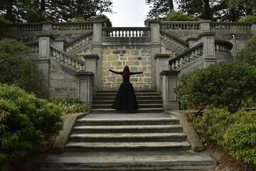 Fototapeta na wymiar portrait of pretty female model with red hair wearing glamorous gothic black lace ballgown. Posing in a fairytale castle location with staircases 