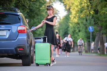Young woman driver taking out suitcase bag out of her car. Travelling and vacations concept