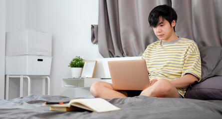 Young man in casual clothes sitting in bed in morning and working with laptop.