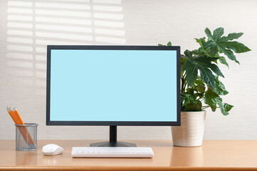 Front view of simple workspace with modern computer and office supplies. Blank screen for your text or advertising content. Plant