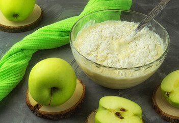 There are fresh green apples on the rustic table, as well as a plate in which flour, eggs, sugar and milk are combined
