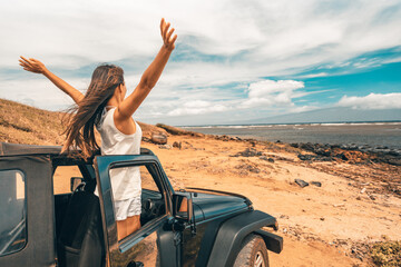 Fototapeta Car road trip travel fun happy woman tourist with open arms at ocean view from sports utility car driving on beach. Summer vacation adventure girl from the back. obraz